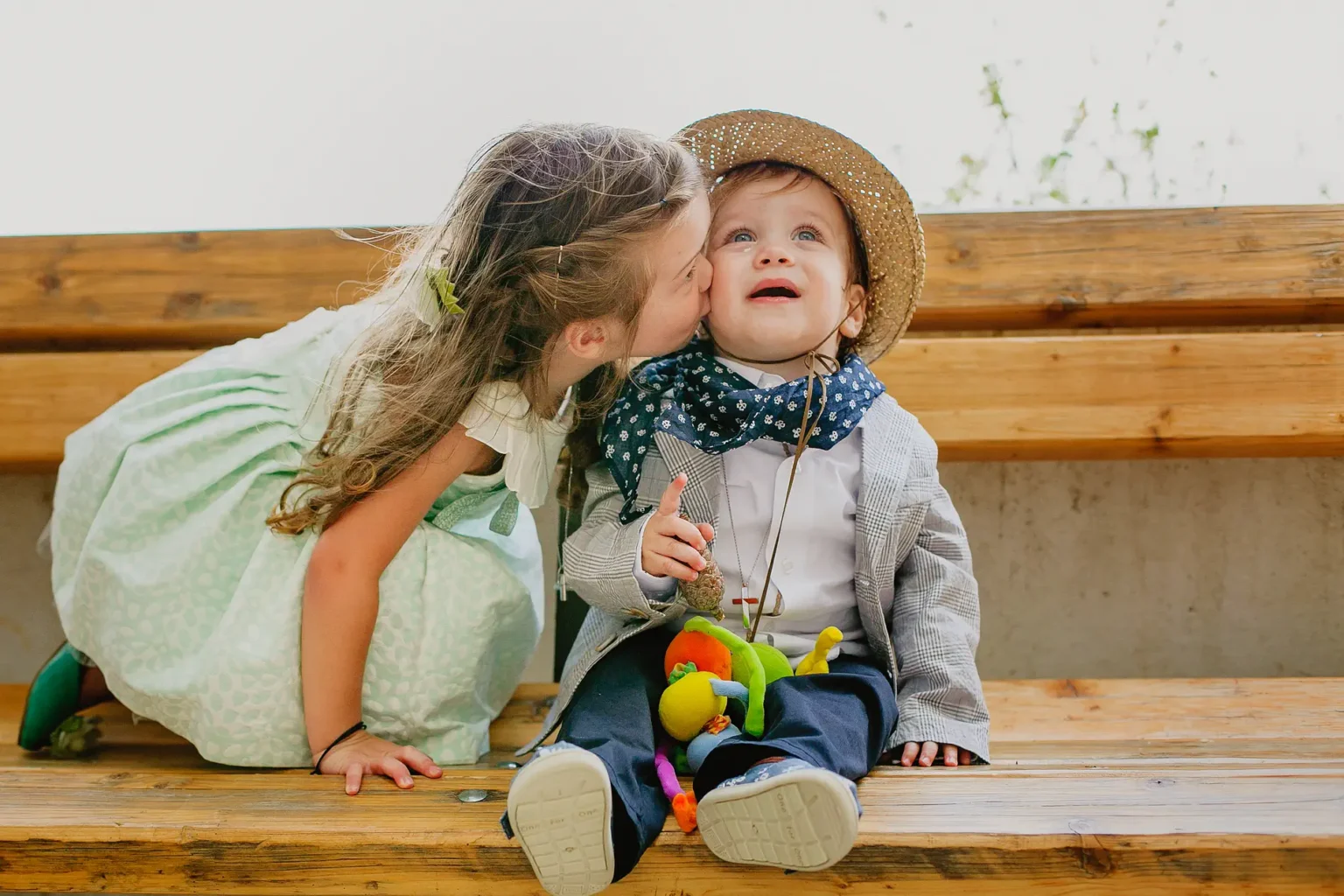 a girl kissing a baby on a bench