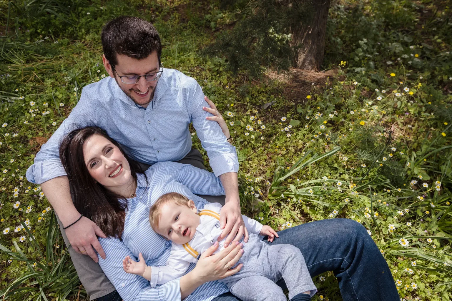 a man and woman sitting on grass with a baby