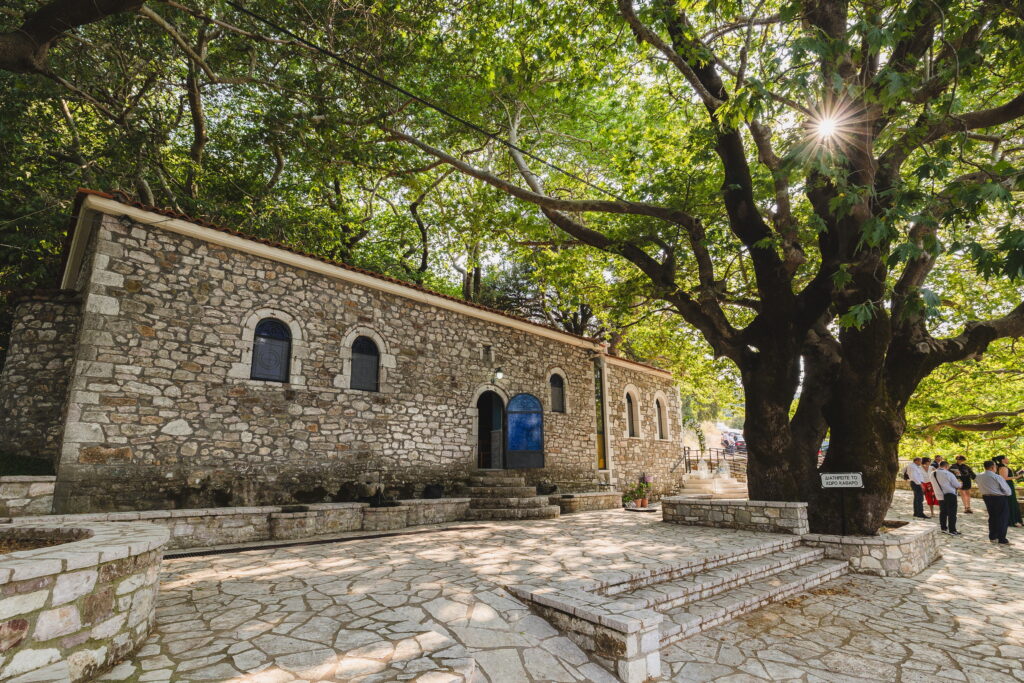 Πέτρινη εκκλησία κάτω από ένα μεγάλο πλατάνι σε μια πλακόστρωτη αυλή