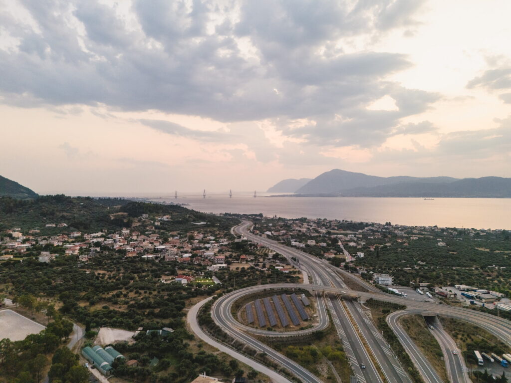 Κόμβος αυτοκινητόδρομου με φωτοβολταϊκά, παραθαλάσσια πόλη και η γέφυρα Ρίου-Αντιρρίου στο βάθος